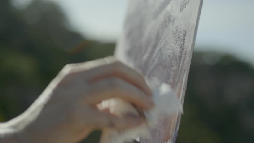 A woman wearing a hat is painting onto a canvas held up by an easel atop a mountain