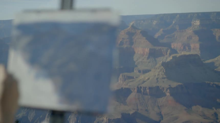 A woman stands on top of a hill and paints the landscape below her