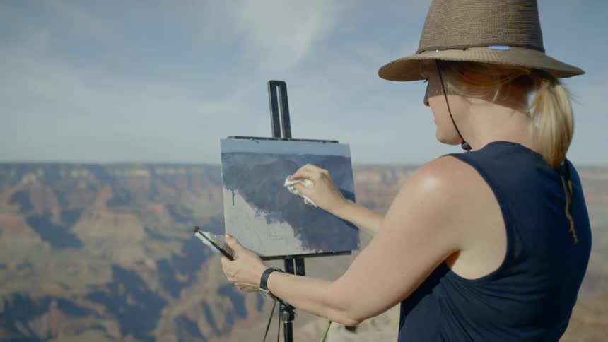 Artist works on her canvas outdoors in front of mountains and mesa