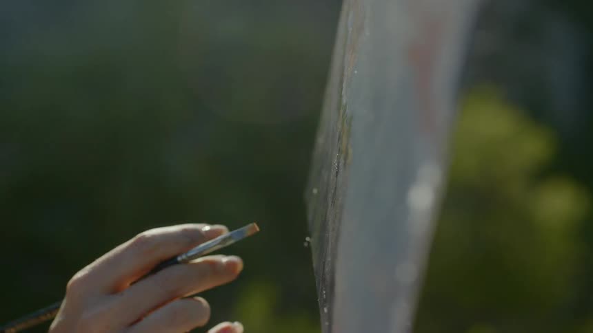 A woman wearing a hat is painting onto a canvas held up by an easel atop a mountain