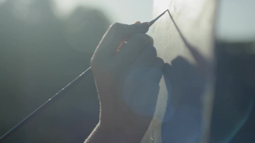 A woman wearing a hat is painting onto a canvas held up by an easel atop a mountain
