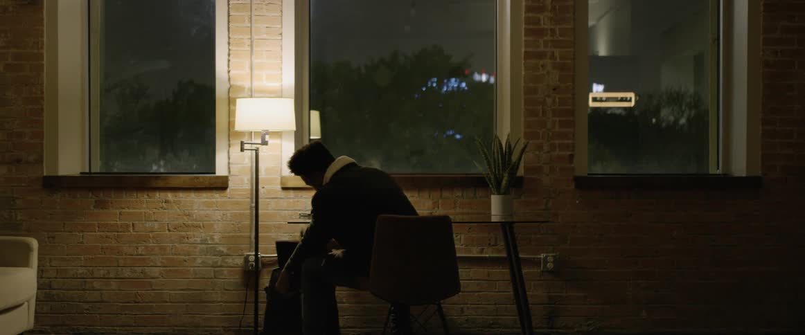 Man enters a room carrying a backpack and sits at a table and removes a laptop from the backpack