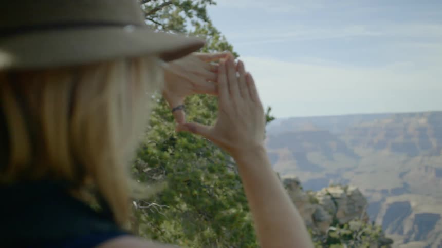A blonde woman frames a canyon view with her hands