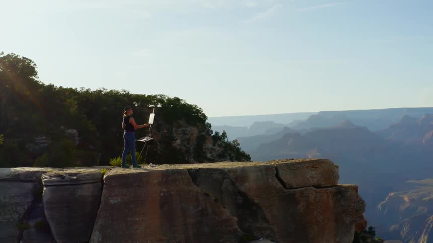 A woman is painting by the cliff