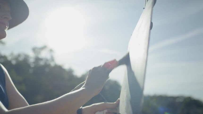 A woman wearing a hat is painting onto a canvas held up by an easel atop a mountain