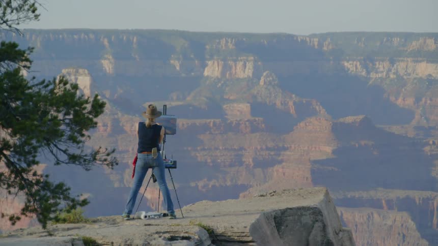 A painter making a landscape portrait while standing on the ledge of canyon