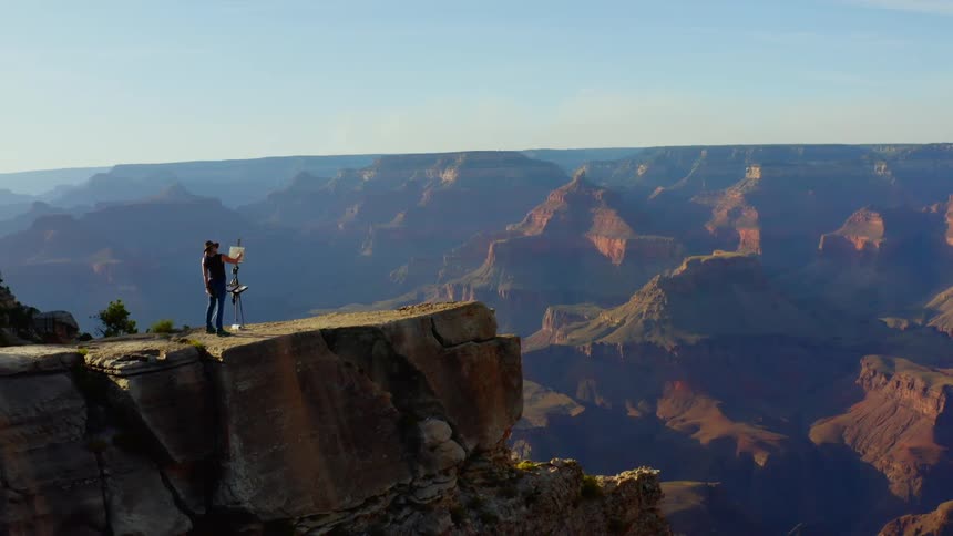 A person paints while standing on the rim of the grand canyon