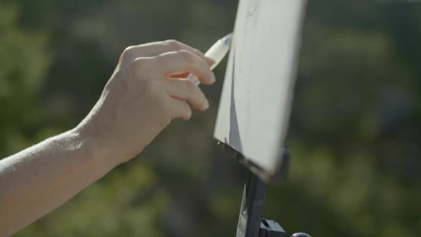 An artist sketches outside on a canvas on an easel