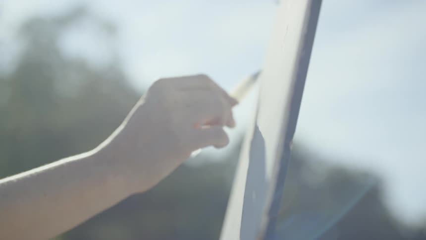 A woman wearing a hat is painting onto a canvas held up by an easel atop a mountain