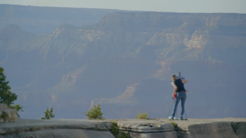 A woman stands on the ledge of a cliff and paints the landscape in front of her