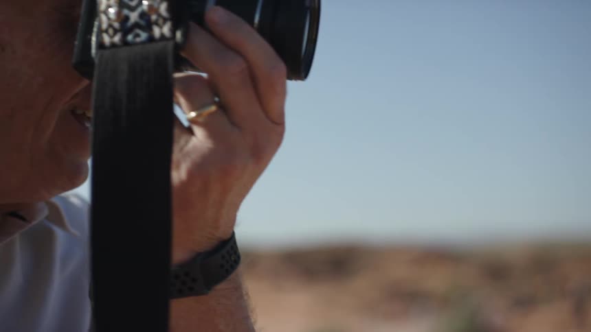 A man with a camera to his eye standing and smiling