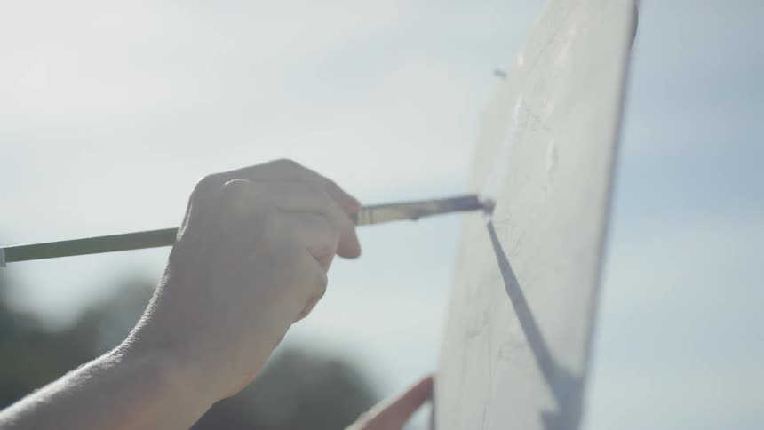 A woman wearing a hat is painting onto a canvas held up by an easel atop a mountain