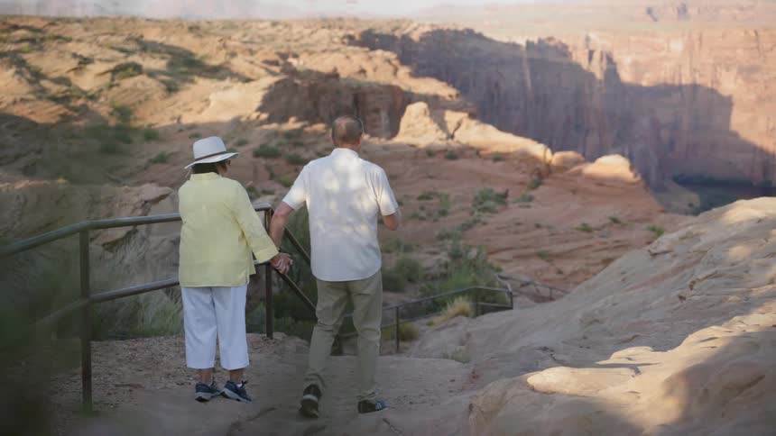 A man and woman hold hands crossing a high rocky terrain