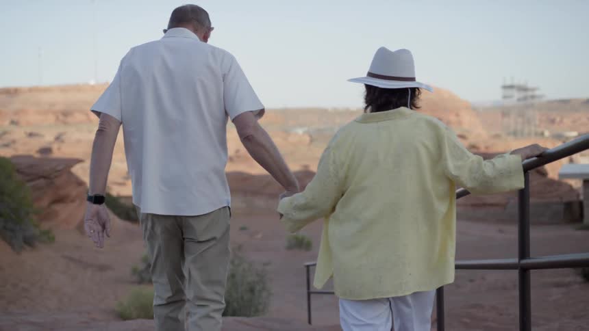 A man and woman hold hands as they walk down a ramp in the desert
