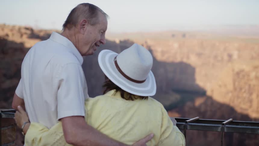 An older couple kiss as they stand on observation point looking down on canyon