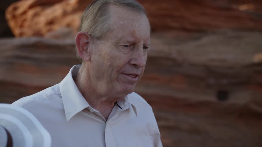 An old man talks while he stands in front of a rock formation