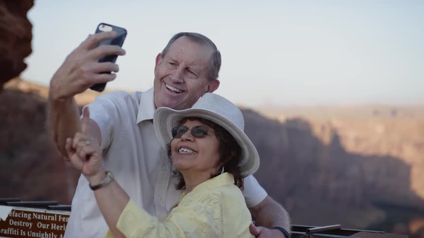 A man holding up his phone and hugging his wife takes a selfie with the canyon behind them