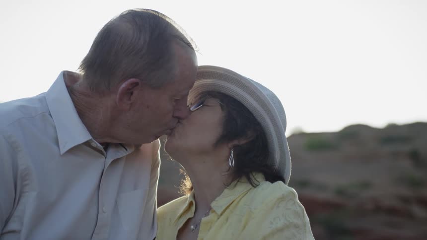 A man and woman kiss while standing under the sun