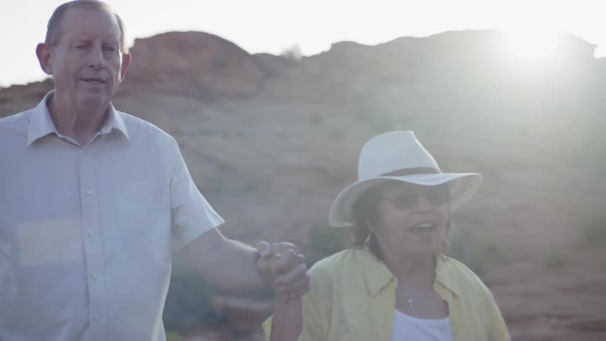 An elderly man and woman walk outside holding hands