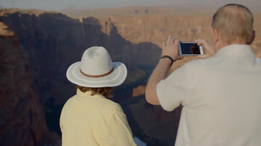 An old white couple take a picture of a deep canyon