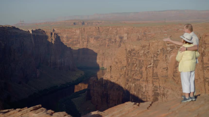An elderly couple embrace standing at the top of a canyon
