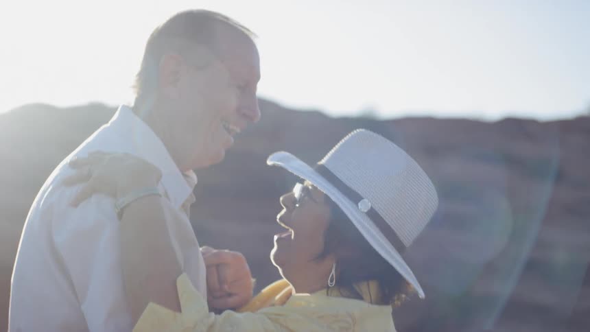 Older couple dance outside near rocky hill under bright sunshine