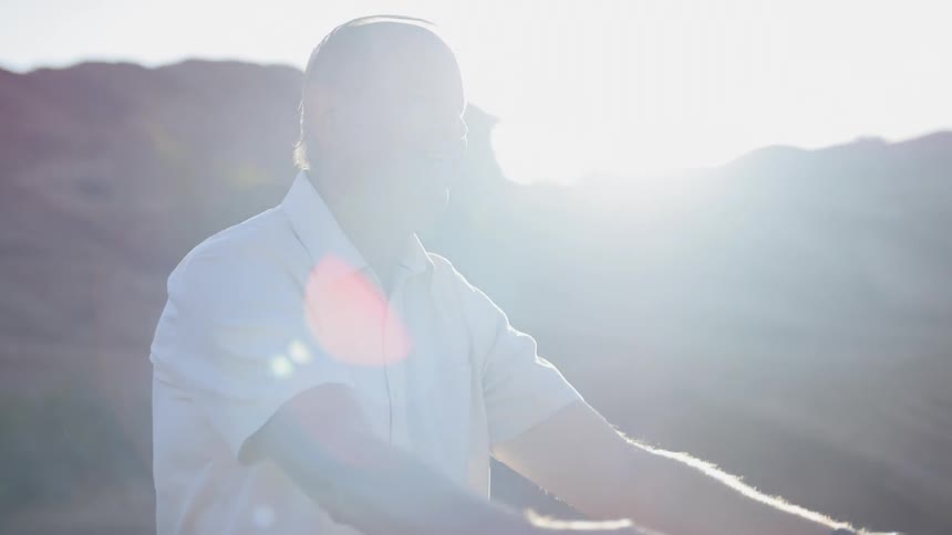 A man and a woman dancing outside with a cliff and the sun in the background