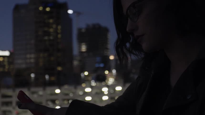 A woman looks at her phone while outside in a city at night