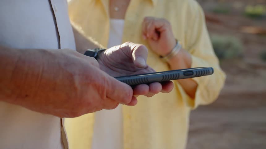 Senior man standing next to the woman uses smartphone during daylight
