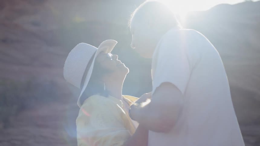 An elderly man and woman dance and kiss in front of a canyon