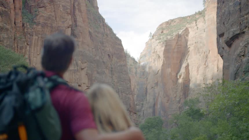 A man and a woman stand outdoors and look at tall cliffs