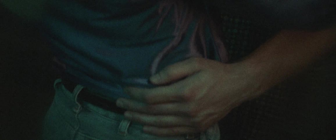 A woman in a western style shirt is dancing slowly with a man in a dimly lit space
