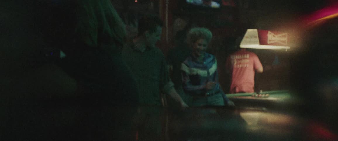 A couple line dances in a country bar while others play pool