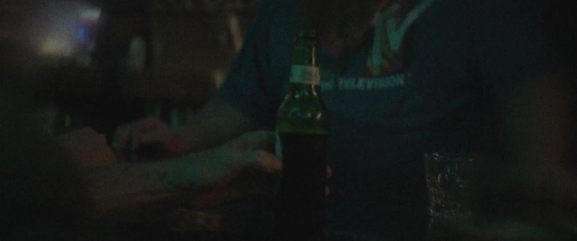 A person has their hand on a beer bottle touching the label in a dark room