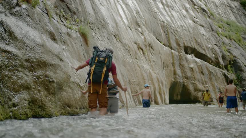 People walking in a river next to a cliff