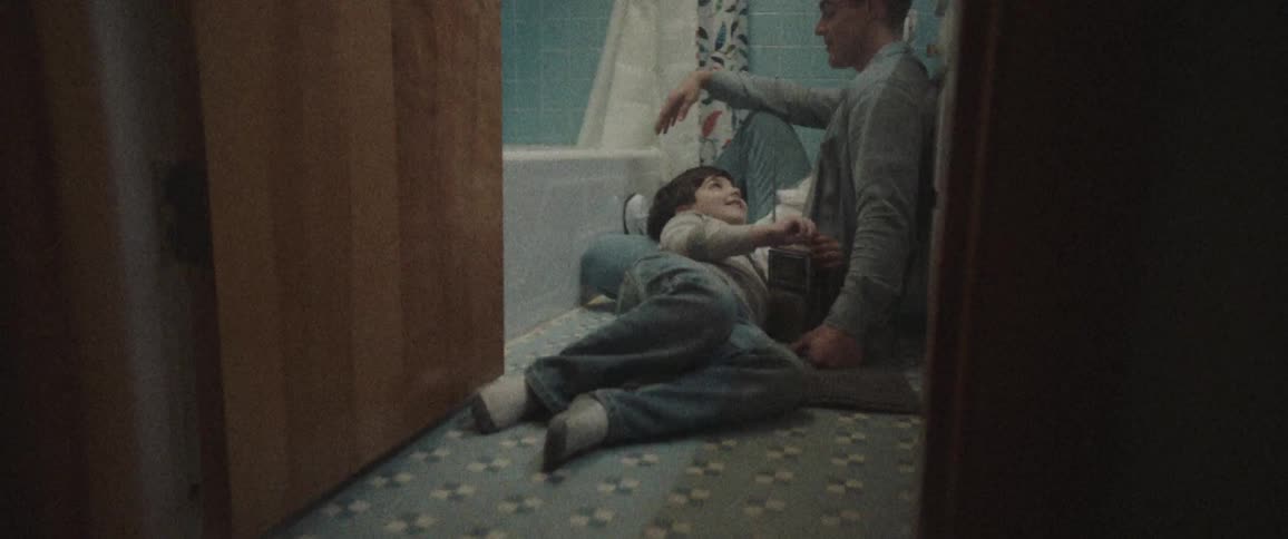 A young boy lays on the floor of a bathroom with his head resting on his fathers leg as they enjoy time together listening to the radio