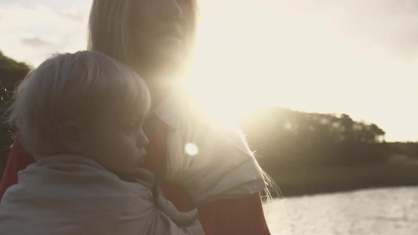 Woman holding her baby standing next to water