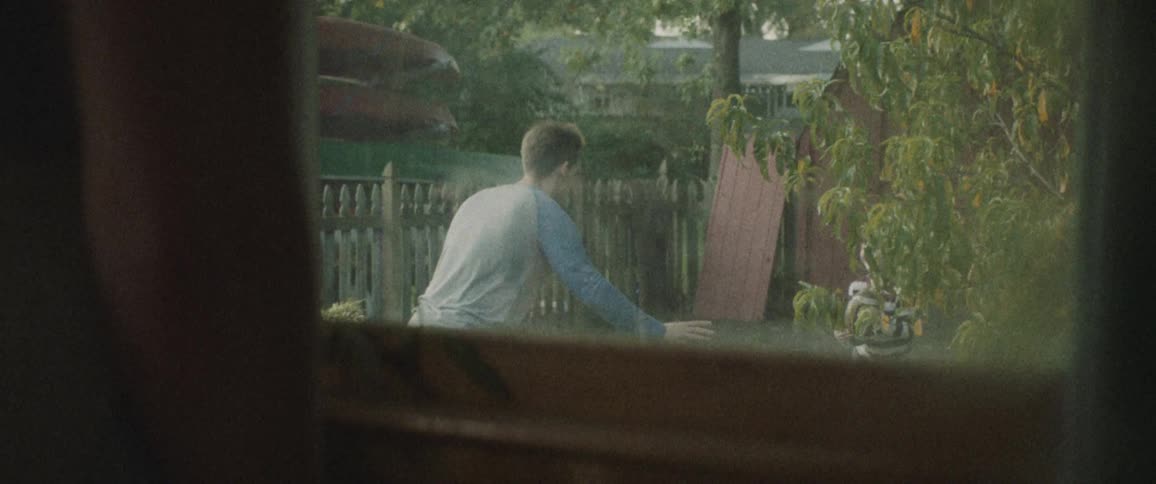 Someone watches out the window as a man and little boy throw a football together