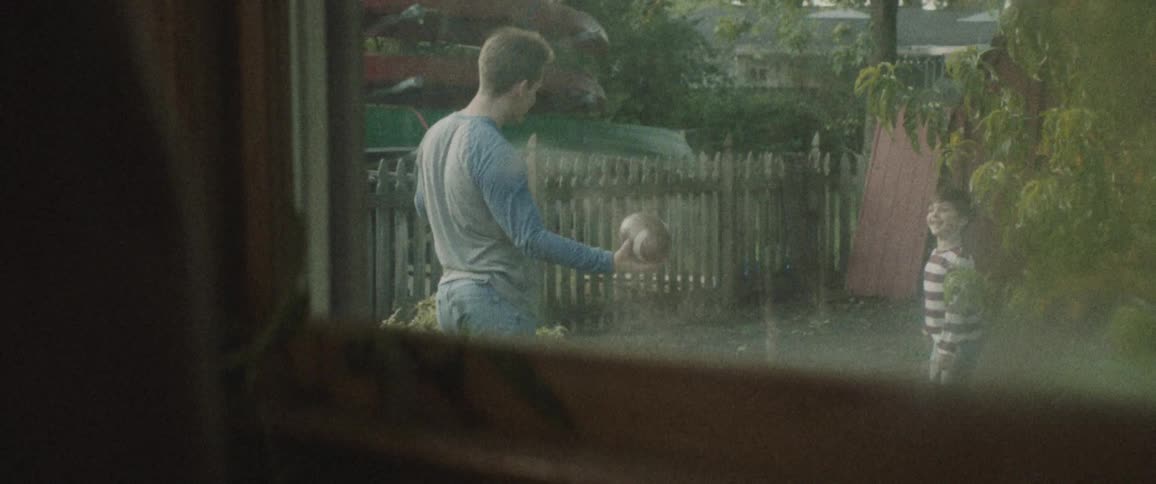 A woman watches a father and son throw a football around outside in their yard