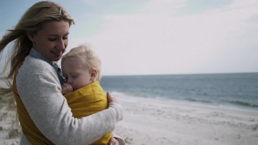 A woman holds a baby near the ocean