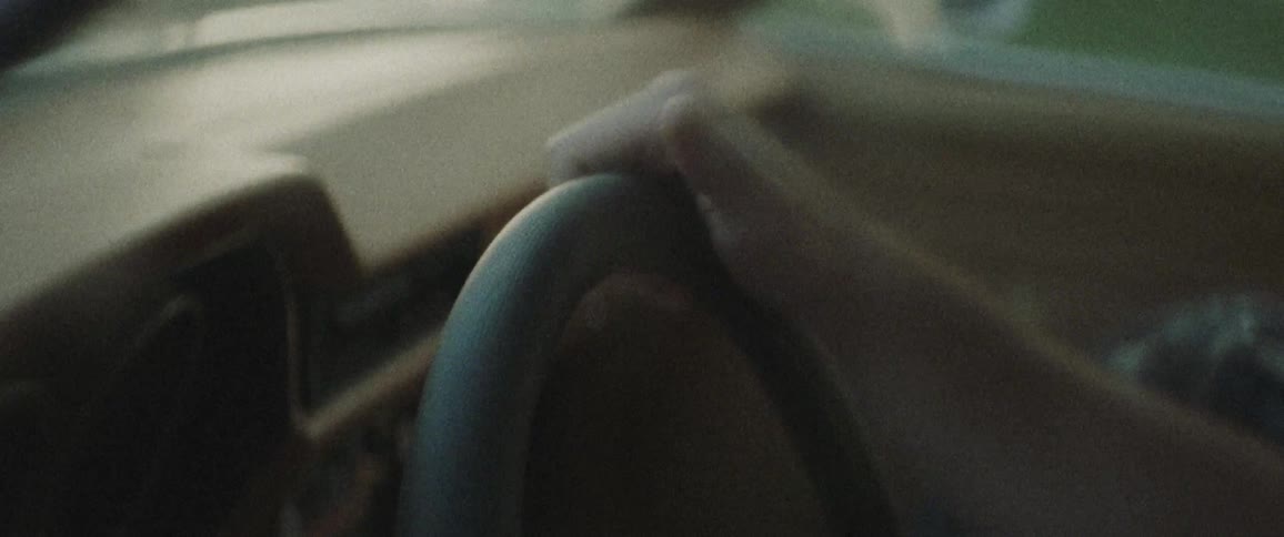 A man sits in a car and taps his thumb on the steering wheel