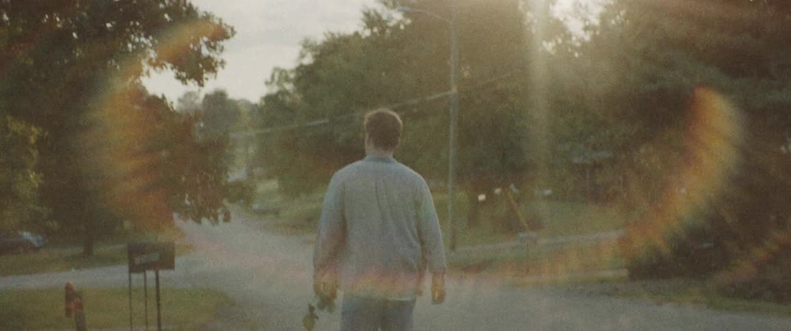 Man holding a rose walks on the road during daylight