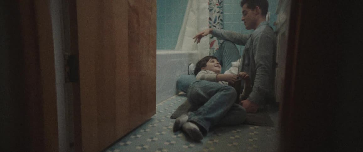 A child lies on the bathroom floor with his head in his dads lap looking up and talking
