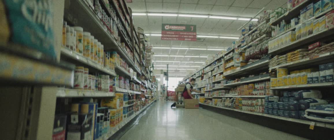 Grocery clerk kneels in grocery aisle stocking shelf