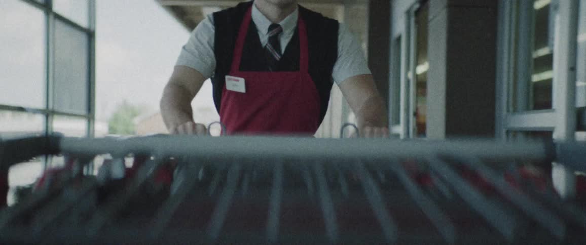 A man with a red apron and name tag pushing a shopping cart then going into a store