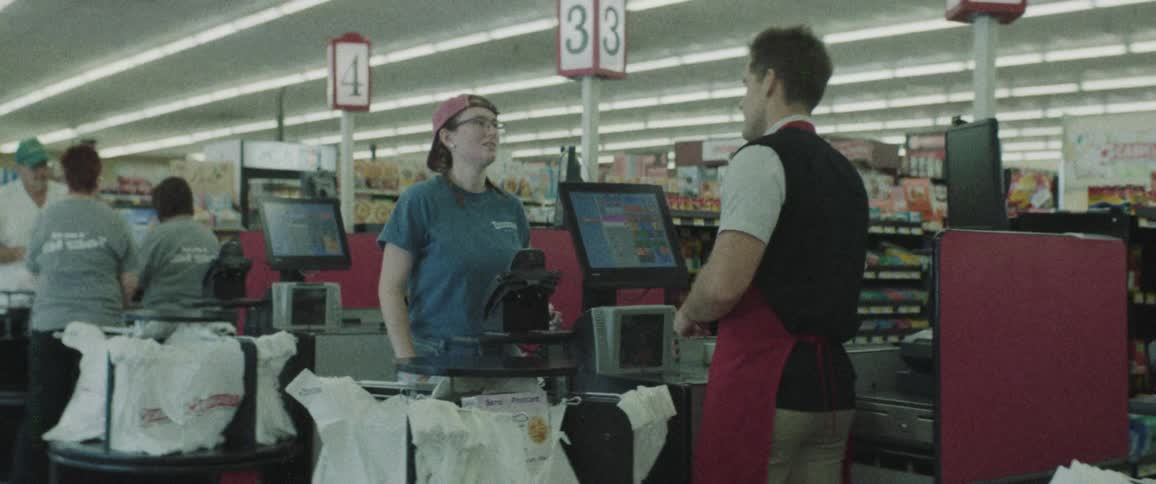 A cashier scanning and bagging groceries while talking to a customer
