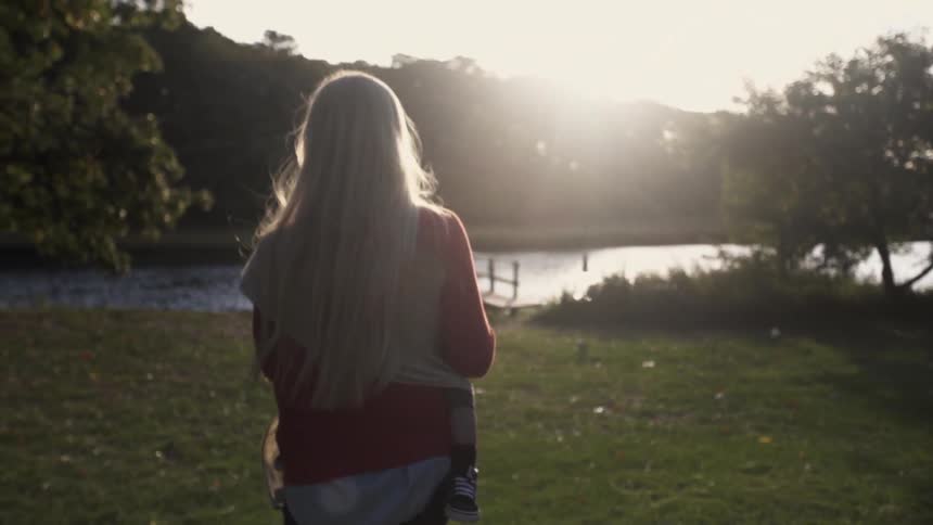 A woman with long blonde hair walking in a field near a lake