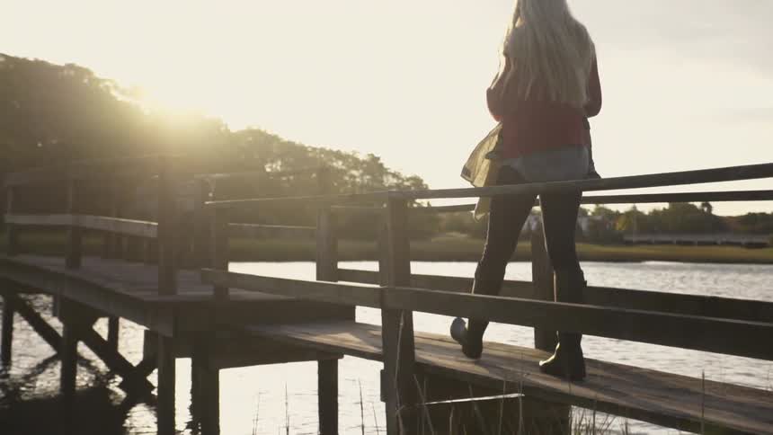 A woman holding a baby walks on the deck as the sun sets