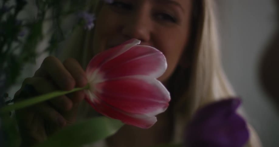 A woman is smiling as she smells some flowers