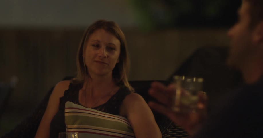 A woman laughing at something a man holding a drink glass is saying to her as light flickers over them